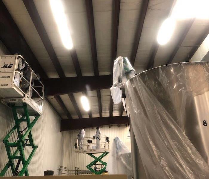 SERVPRO techs on cherry pickers cleaning walls in manufacturing plant